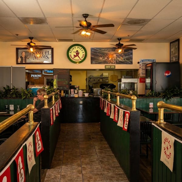 Interior of a casual pizza restaurant with green booths, brass railings, and a counter in the back.