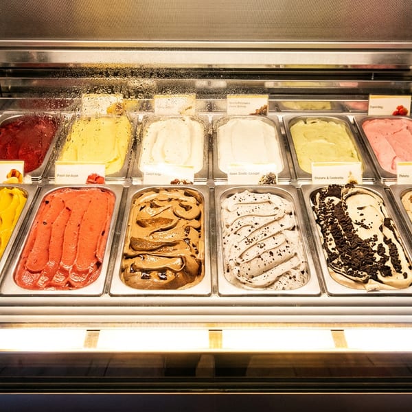 A brightly lit display case filled with various colorful gelato flavors, including chocolate, strawberry, and vanilla.