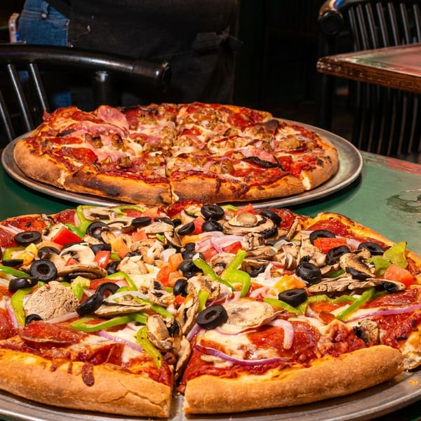 Two pizzas, one with pepperoni and vegetables, the other with meat, on a table with a beer.