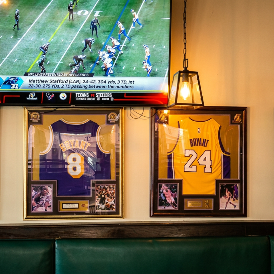 Framed Lakers jerseys of James, Bryant, and West hang below a TV showing a football game.